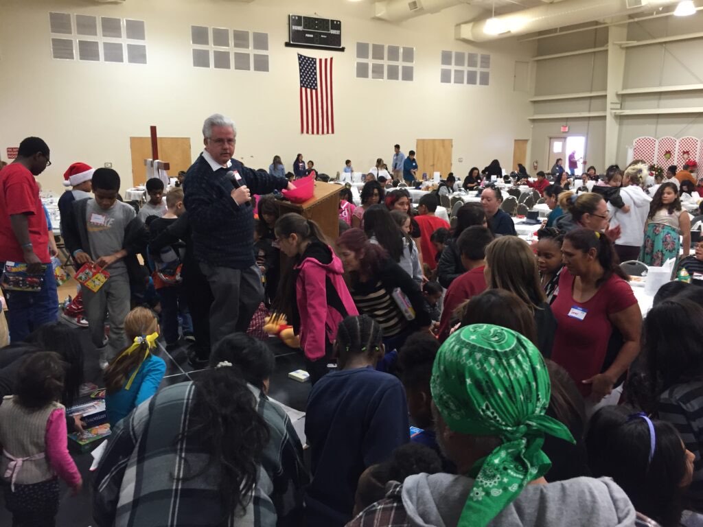A packed fellowship hall at the Angel Tree Christmas party, kids holding wrapped gifts