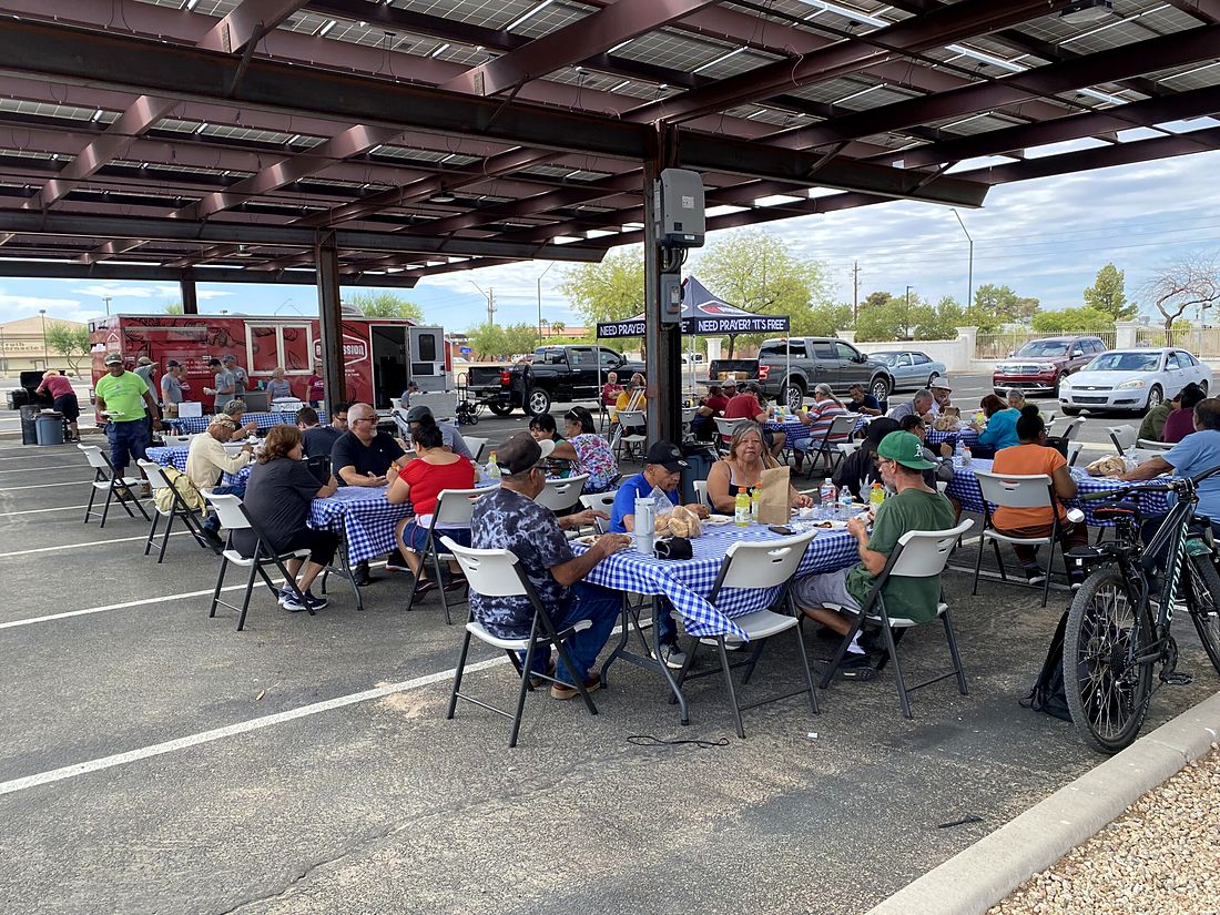 Neighbors sharing the free Wednesday lunch at tables in the church parking lot