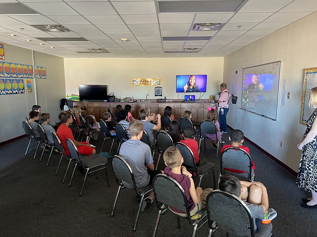 Children in chairs watching a lesson on a screen