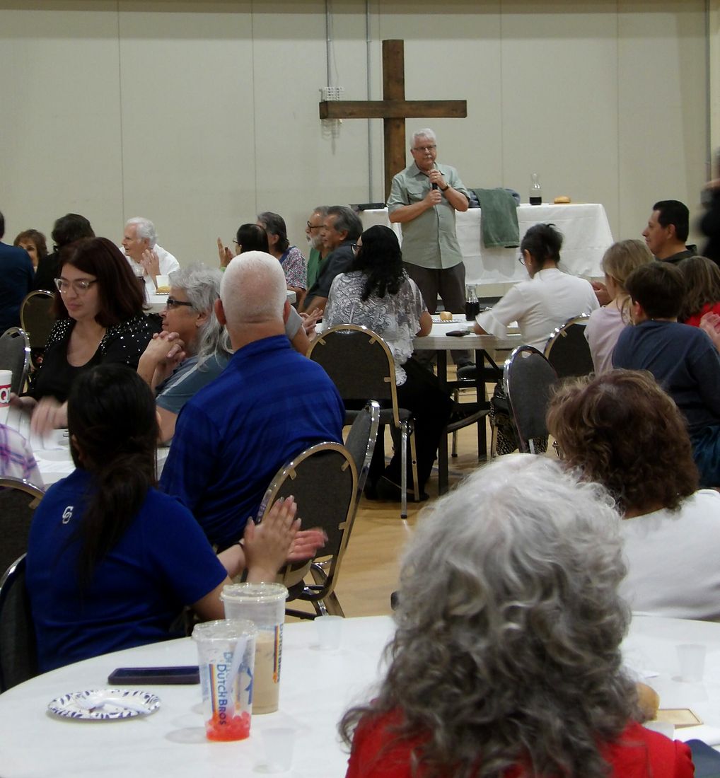 Members seated at round tables for the Lord’s Supper, the cross on the wall behind